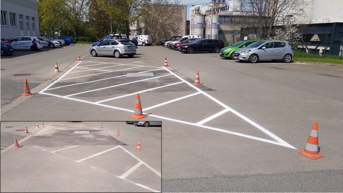 Weiße Fahrbahnmarkierung mit schraffierter Sperrfläche auf Asphalt, abgesichert mit Pylonen